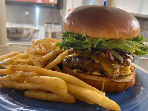 A juicy burger with lettuce, cheese, and bacon, served with a side of golden French fries on a blue plate.