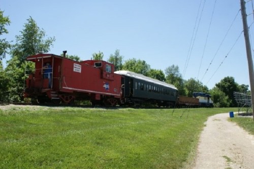 A red caboose and a black train car on a sunny day, surrounded by green trees and grass along a railway track.