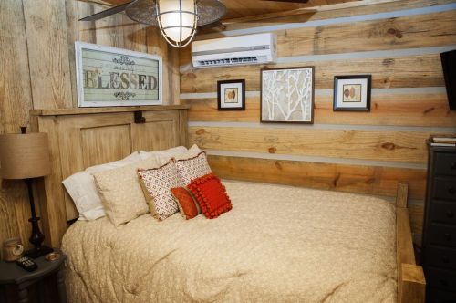 Cozy bedroom with wooden walls, a bed with decorative pillows, and framed art on the wall.