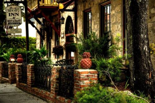 Charming inn exterior with brick walls, lush greenery, and decorative pineapples near a sign for dining and lodging.