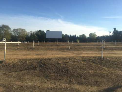 A vacant outdoor movie theater with a large blank screen and empty parking area under a clear blue sky.
