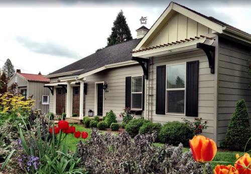 A charming gray house with a well-kept garden featuring colorful flowers and shrubs under a cloudy sky.