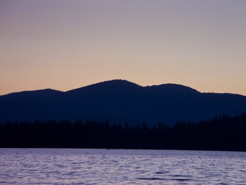 Silhouette of mountains against a twilight sky, reflecting on calm water below.