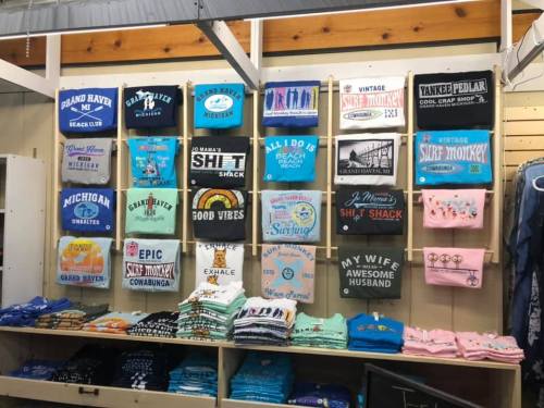 A display of colorful t-shirts and sweatshirts on racks, featuring various fun and humorous designs and slogans.