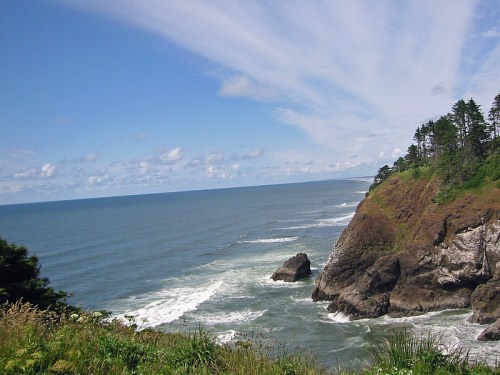 A scenic coastal view with cliffs, waves crashing, and a blue sky with wispy clouds.