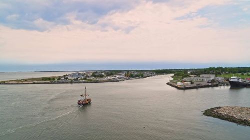 A boat navigates a calm waterway, surrounded by a coastal town and lush greenery under a cloudy sky.