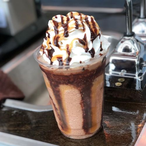 A delicious chocolate milkshake topped with whipped cream and drizzled with chocolate syrup in a clear cup.