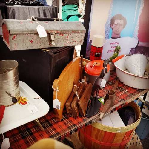 A table filled with vintage items, including a toolbox, wooden utensils, and a bowl, set against a plaid tablecloth.