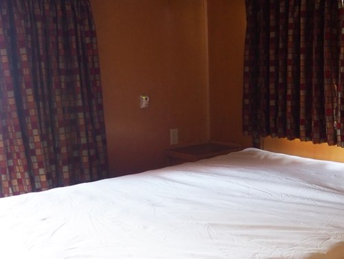A simple bedroom with a bare bed and patterned curtains on the windows.