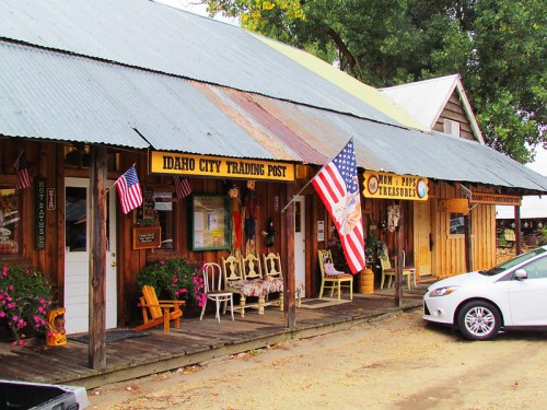 A rustic trading post with American flags, colorful flowers, and wooden structures in Idaho City.