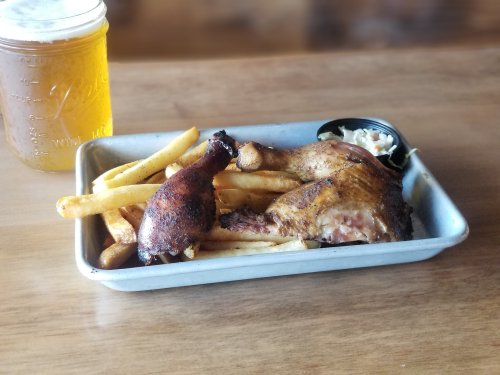 A plate of crispy fried chicken with fries and coleslaw, alongside a jar of beer on a wooden table.