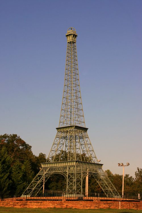 A replica of the Eiffel Tower stands tall against a clear blue sky, surrounded by trees and park lighting.