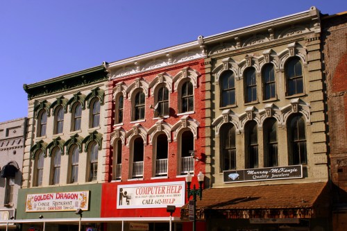 Historic buildings with ornate facades in various colors, featuring shops on the ground level and balconies above.