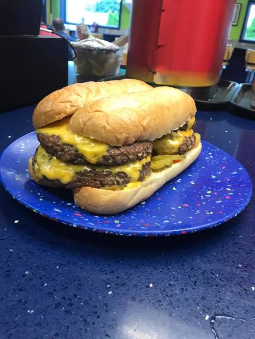 A large sandwich with two beef patties and melted cheese, served on a soft bun, on a colorful plate.