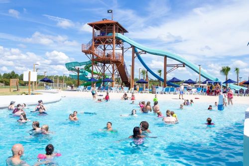 A vibrant water park scene with a large water slide, people swimming in a pool, and sunny skies.