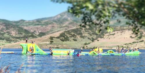 A group of people enjoying inflatable water attractions on a lake surrounded by green hills.