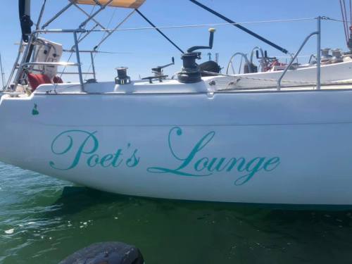 A close-up of a sailboat's side featuring the name "Poet's Lounge" in elegant turquoise lettering.