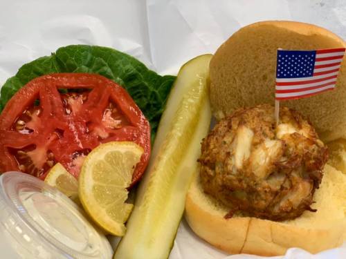 A sandwich with a small American flag, lettuce, tomato, and lemon slices on a plate.