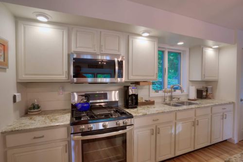 Modern kitchen with white cabinets, granite countertops, stainless steel appliances, and a window overlooking greenery.