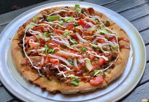 A pizza topped with lettuce, tomatoes, onions, pickles, and sauces on a wooden table.