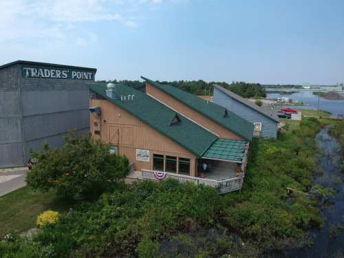 Aerial view of Traders' Point building surrounded by greenery and water, with a blue sky in the background.