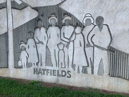 A carved mural depicting a group of people, labeled "HATFIELDS," with various figures in different poses.