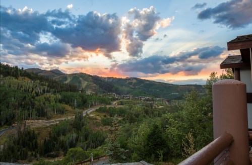 A scenic view of mountains and trees under a colorful sunset with clouds, showcasing a peaceful landscape.