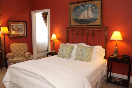 Cozy bedroom with a brass bed, decorative pillows, and warm lighting against a red wall, featuring a sailboat painting.