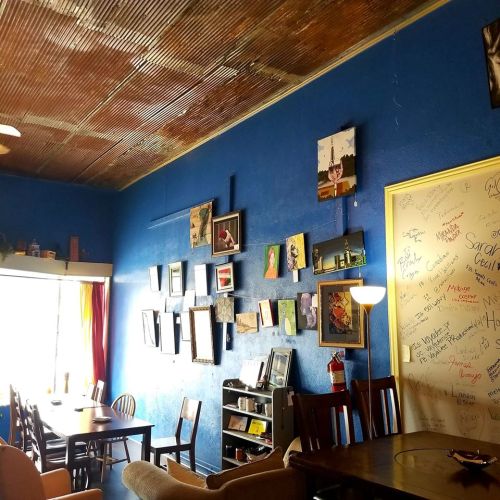 Cozy café interior with blue walls, artwork on display, wooden tables, and a warm, inviting atmosphere.