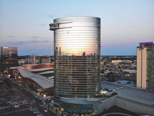 A modern glass skyscraper reflecting the sunset, surrounded by city buildings and a bustling urban landscape.