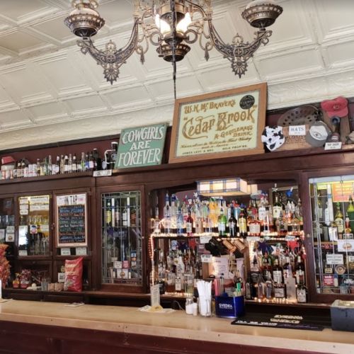 A vintage bar with a wooden counter, shelves filled with various bottles, and decorative signs on the wall.