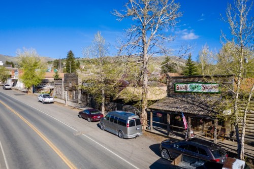 A historic street scene featuring old wooden buildings, a saloon, and parked cars under a clear blue sky.