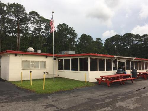 A small, one-story building with a red roof, surrounded by trees, featuring outdoor seating and an American flag.