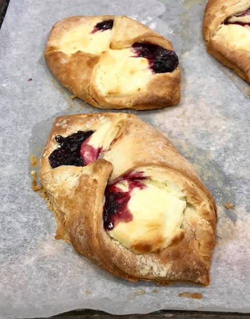 Two baked pastries with a golden crust, filled with cream cheese and berry jam, resting on parchment paper.