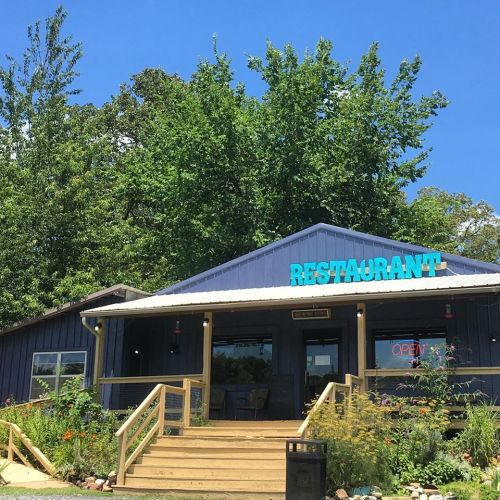 A blue restaurant building with a sign that says "RESTAURANT" and an "OPEN" sign, surrounded by greenery.