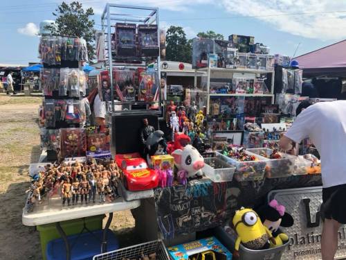 A vibrant outdoor market stall filled with various toys, action figures, and collectibles under a clear blue sky.