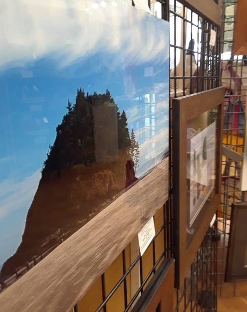 A landscape photograph of a rocky hill with trees, displayed in a gallery setting with other framed images nearby.