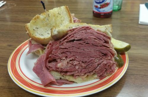 A stacked sandwich with layers of deli meat, served on toasted bread with pickles on the side.