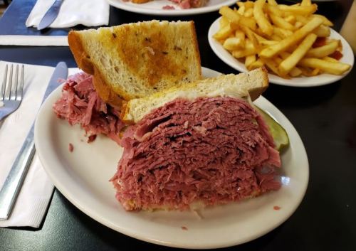 A sandwich filled with piled high corned beef on toasted bread, served with a side of French fries.