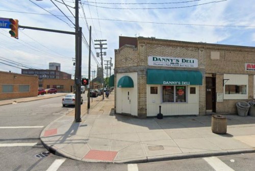 A corner view of Danny's Deli, featuring a green awning and nearby street signs in an urban setting.