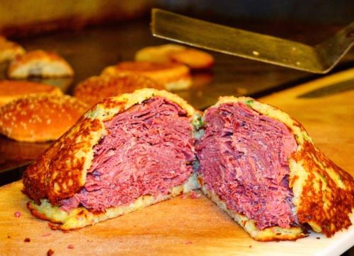 A cross-section of a crispy, golden-brown sandwich filled with layers of pink corned beef on a wooden cutting board.