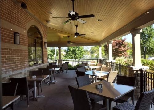 Outdoor dining area with tables and chairs, ceiling fans, and a view of greenery under a covered patio.