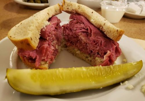 A close-up of a sandwich filled with piled high corned beef, served with a pickle on the side.