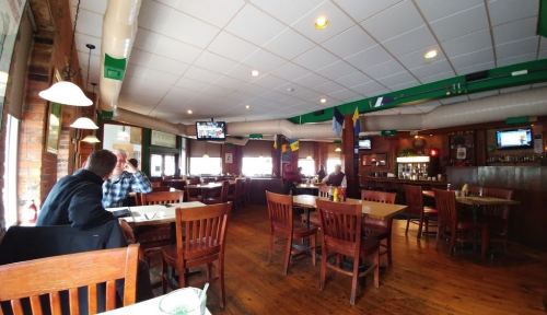 A cozy restaurant interior with wooden tables and chairs, featuring TVs and a few patrons enjoying their meals.
