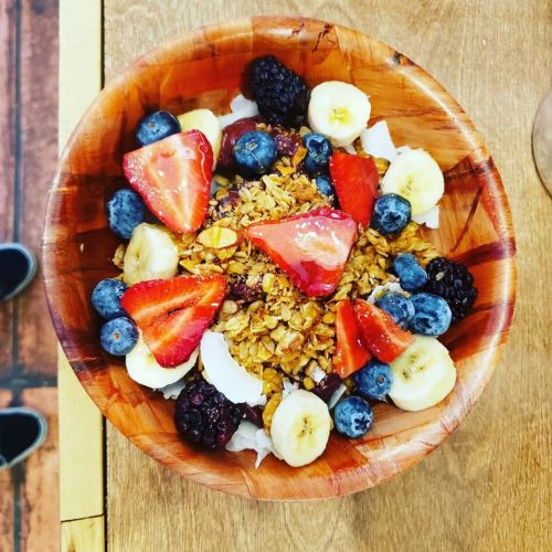A wooden bowl filled with yogurt, granola, strawberries, blueberries, blackberries, and banana slices.