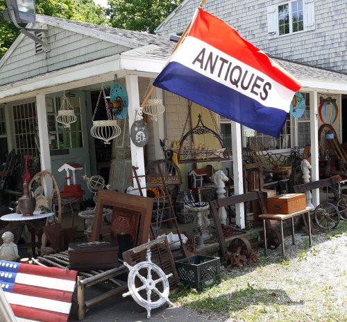 A charming antique shop with a red, white, and blue flag, showcasing various vintage items outside.