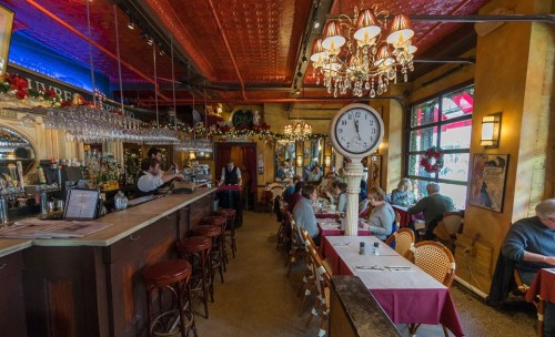 A cozy restaurant interior with a bar, tables, and festive decorations, featuring a large clock and patrons dining.