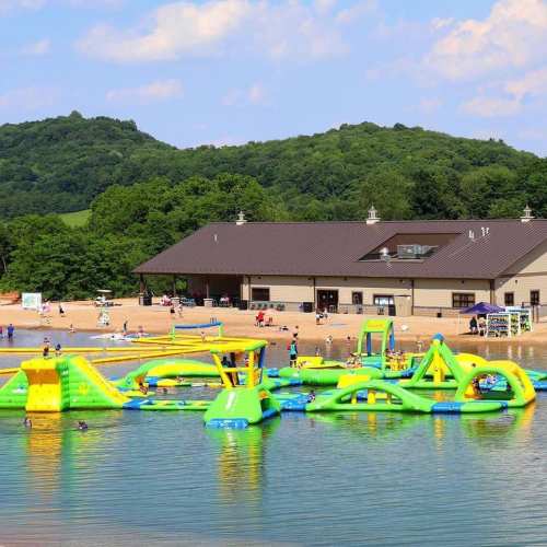 A vibrant beach scene with inflatable water attractions, a sandy shore, and a building surrounded by green hills.