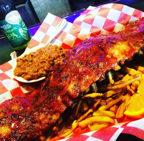 A plate of BBQ ribs with sauce, served with fries and baked beans, all in a red-checkered basket.