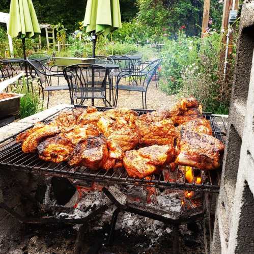 Grilled chicken pieces sizzling on a barbecue, surrounded by a lush garden and outdoor seating.